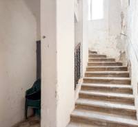 Rodinný dom (bytovka) s pozemkom 554m2, Bobotská Lehota - Schodisko v rodinnom dome so stohom plastových stoličiek. Opotrebované steny.