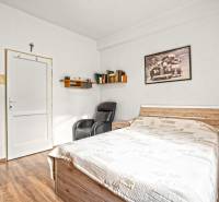 NA PREDAJ VÝNIMOČNÝ RODINNÝ DOM VO VEĽKOM MEDERI - Izba v rodinnom dome s posteľou, kreslom a policou, podlaha s dreveným dekorom.