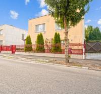 NA PREDAJ VÝNIMOČNÝ RODINNÝ DOM VO VEĽKOM MEDERI - Rodinný dom vo Veľkom Mederi s červeným plotom a stromami v predzáhradke.