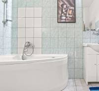 NA PREDAJ VÝNIMOČNÝ RODINNÝ DOM VO VEĽKOM MEDERI - Kúpeľňa v rodinnom dome s rohovou vaňou a umývadlom na svetlej dlažbe.