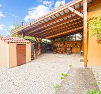 NA PREDAJ VÝNIMOČNÝ RODINNÝ DOM VO VEĽKOM MEDERI - Záhrada rodinného domu vo Veľkom Mederi s prístreškom a drevným dekorom na stene.