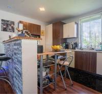 NA PREDAJ 3 IZBOVÝ RODINNÝ DOM, KĽÚČIAROVÉ KRAČANY - Kuchyňa v rodinnom dome s barovým pultom a podlahou s dreveným dekorom.