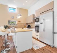 NA PREDAJ NADŠTANDARDNÁ 4-IZB. NOVOSTAVBA, DUN. KLÁTOV - Kuchyňa v rodinnom dome s bielymi skrinkami, barovými stoličkami a vstavanými spotrebičmi.