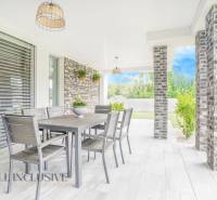 NA PREDAJ NADŠTANDARDNÁ 4-IZB. NOVOSTAVBA, DUN. KLÁTOV - Terasa rodinného domu v Dunajskom Klátove s jedálenským stolom a záhradnými rastlinami.