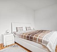 NA PREDAJ APARTMÁNOVÝ DOM VO VEĽKOM MEDERI - Svetlá spálňa s veľkou posteľou, podlahou s dreveným dekorom a nočným stolíkom.