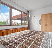 NA PREDAJ APARTMÁNOVÝ DOM VO VEĽKOM MEDERI - Spálňa s veľkým oknom, drevenou skriňou a posteľou v hoteloch a penziónoch.