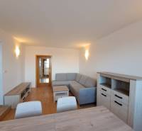 Prenájom pekného a priestranného 4-izbového bytu vo Svite - Obývacia izba v 4-izbovom byte s podlahou s dreveným dekorom a sivou sedačkou.