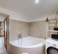 Rodinný dom Unín s pozemkom 941 m2 - Kúpeľňa v rodinnom dome s rohovou vaňou, práčkou a kvetmi.