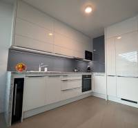 Exk. prenájom lux. 2 iz bytu Rezidencia Blumental - Moderná kuchyňa v 2-izbovom byte s podlahou s dreveným dekorom a bielymi skrinkami.