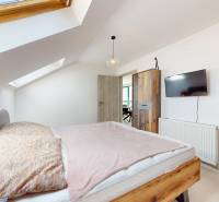 Krásny moderný 2 izbový byt v centre Bratislavy, nám. SNP - Podkrovná spálňa v 2-izbovom byte, drevená posteľ, strešné okná, televízor na stene.