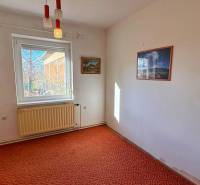 NA PREDAJ 5 izbový rodinný dom s veľkou záhradou v obci Iža - Izba v rodinnom dome, kobercom pokrytá podlaha, biely radiátor, obrazy na stenách.