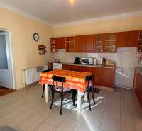 NA PREDAJ 5 izbový rodinný dom s veľkou záhradou v obci Iža - Kuchyňa v rodinnom dome s dreveným dekorom a oranžovým obrusom na stole.