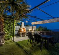 Kaštela(HR)-moderná vila s krásnym výhľadom - Palmová záhrada vily v Kaštela s pergolou, krbom a stolom.