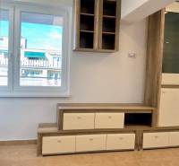 I Predaj Investičného 1-izbového bytu s veľkorysou loggiou  - Obývacia stena v 1-izbovom byte s podlahou s dreveným dekorom a výhľadom z okna.