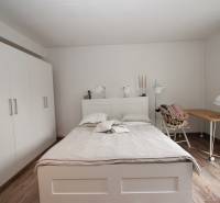 1-izb. kompletne zrekonštr.byt na Hradnom kopci (Lichardova ul.)  - Spálňa v 1-izbovom byte s posteľou, bielou skriňou a podlahou s dreveným dekorom.