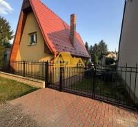 Predám peknú chatu na celoročné bývanie v Nových zámkoch - Chata na ulici v Nových Zámkoch, so špicatou strechou a tehlovým komínom.