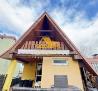 Predám peknú chatu na celoročné bývanie v Nových zámkoch - Drevená chata s terasou v Nových Zámkoch pod modrým oblohou.