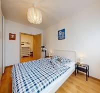 Na predaj moderný 3i byt v novostavbe Ovocné sady s parkovaním, BA - Spálňa v 3-izbovom byte s posteľou, nočnými stolíkmi a podlahou s dreveným dekorom.