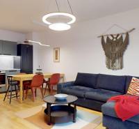 Na predaj moderný 3i byt v novostavbe Ovocné sady s parkovaním, BA - Obývačka s kuchyňou v 3-izbovom byte, pohovka, stôl, kuchynská linka, podlaha s dreveným dekorom.