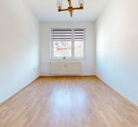 Predaj, trojizbový byt v Kremnici - Prázdna miestnosť s podlahou s dreveným dekorom v 3-izbovom byte, jednoduché steny a okno.