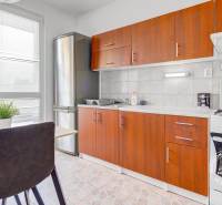 4-i., zariadený, lodžia, pivnica, internet, Röntgenova ul. - Kuchyňa 4-izbového bytu so stolom, stoličkami, sporákom, chladničkou a hnedými skrinkami.