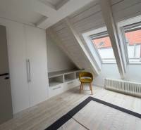 4 Izbový byt na Medenej ulici na prenájom - Podkrovná izba s podlahou s dreveným dekorom, vstavanou skriňou a žltou stoličkou.