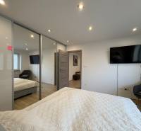 NA PREDAJ vkusne zrekonštruovaný  2 izbový byt, Komárno - Spálňa v 2-izbovom byte s televízorom, veľkou skriňou a podlahou s dreveným dekorom.