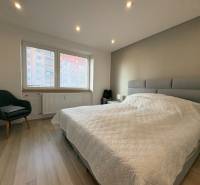 NA PREDAJ vkusne zrekonštruovaný  2 izbový byt, Komárno - Spálňa v 2-izbovom byte s podlahou s dreveným dekorom, pohodlným kreslom a veľkým oknom.