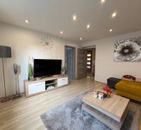 NA PREDAJ vkusne zrekonštruovaný  2 izbový byt, Komárno - Obývačka v 2-izbovom byte s podlahou s dreveným dekorom, TV a žltou pohovkou.