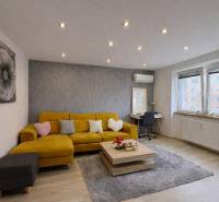 NA PREDAJ vkusne zrekonštruovaný  2 izbový byt, Komárno - Obývacia izba v 2-izbovom byte s pohovkou, podlaha s dreveným dekorom, šedý koberec.