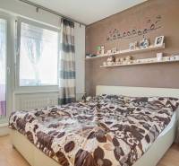 3-izbový byt s loggiou na ul. S.H. Vajanského, Nové Zámky – 74,69m2 - Spálňa v 3-izbovom byte s dekoratívnou stenou, poličkou a posteľou, podlaha s dreveným dekorom.