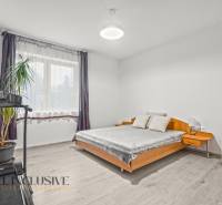 REZERVOVANÉ 5-IZBOVÝ RODINNÝ DOM VO VEĽKEJ PAKE - Svetlá spálňa s posteľou, bežeckým pásom, rastlinou a podlahou s dreveným dekorom v rodinnom dome.