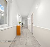 REZERVOVANÉ 5-IZBOVÝ RODINNÝ DOM VO VEĽKEJ PAKE - Chodba s podlahou s dreveným dekorom v rodinnom dome, biele steny, nábytok a rastliny.