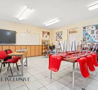 NA PREDAJ ŠKOLSKÁ BUDOVA NA VEĽKOM POZEMKU, MOSTOVÁ - Interiér učebne s červenými stoličkami, školská tabuľa a nástenky na stenách.