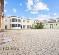 NA PREDAJ ŠKOLSKÁ BUDOVA NA VEĽKOM POZEMKU, MOSTOVÁ - Budova v Mostovej s dláždeným nádvorím a presklenými balkónmi, obloha s oblakmi.