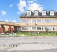 NA PREDAJ ŠKOLSKÁ BUDOVA NA VEĽKOM POZEMKU, MOSTOVÁ - Budova v Mostovej s oknami v podkroví, tehlovými stĺpmi a trávnikom so snehom.