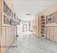 NA PREDAJ ŠKOLSKÁ BUDOVA NA VEĽKOM POZEMKU, MOSTOVÁ - Interiér budovy s trofejami, plagátmi a výstavou fotografií, podlaha s dreveným dekorom.