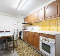 Na predaj 4-izbový rodinný dom, Gabčíkovo - Kuchyňa v rodinnom dome s drevenými skrinkami a kobercom pri jedálenskom stole.