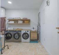 NA PREDAJ 4 IZB RD S DVOJGARÁŽOU, DUNAJSKÁ STREDA - Práčovňa v rodinnom dome s práčkami, poličkou, uterákmi a podlahou s kamenným dekorom.