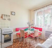 NA PREDAJ 4-IZBOVÝ RODINNÝ DOM NA PRIESTRANNOM POZEMKU - Kuchyňa v rodinnom dome s retro nábytkom, stôl, stoličky, varič, okno so závesmi.