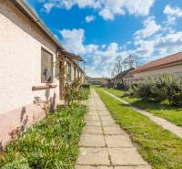 NA PREDAJ 4-IZBOVÝ RODINNÝ DOM NA PRIESTRANNOM POZEMKU - Chodník vedľa rodinného domu s upravenou záhradou a slnečným nebom.
