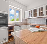 REZERVOVANÉ 3-IZBOVÝ RODINNÝ DOM V OBCI BALOŇ - Kuchynský interiér v Rodinnom dome s podlahou s dreveným dekorom, bielymi skrinkami a oknom.