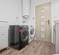 REZERVOVANÉ 3-IZBOVÝ RODINNÝ DOM V OBCI BALOŇ - Práčovňa v rodinnom dome s práčkou, sušičkou a skrinkou, podlaha s dreveným dekorom.