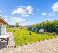 REZERVOVANÉ 3-IZBOVÝ RODINNÝ DOM V OBCI BALOŇ - Záhrada pri rodinnom dome v Baloni s trávnikom a kamenným chodníkom pod modrou oblohou.