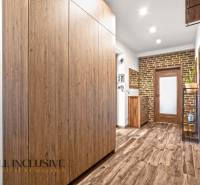 NA PREDAJ 4-IZB NOVOSTAVBA S TROJGARÁŽOU, PIN. KRAČANY - Chodba v rodinnom dome s podlahou s dreveným dekorom, skriňou a tehlovou stenou.