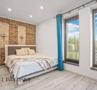 NA PREDAJ 4-IZB NOVOSTAVBA S TROJGARÁŽOU, PIN. KRAČANY - Spálňa v rodinnom dome s tehlovou stenou a výhľadom cez veľké okná.