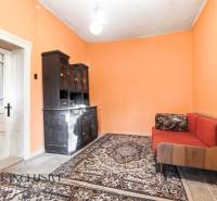Na predaj 4-izbový rodinný dom, Dolné Saliby - Izba v rodinnom dome s oranžovými stenami, koberec, gauč a tmavá skriňa.