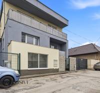 Na predaj 3-izbový byt so záhradkou, Senec - Trojpodlažná budova pri ceste v Senci, obklopená autami a ostatnými budovami. Hotely a penzióny.