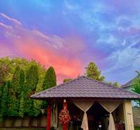 Na predaj 5-izb. rodinný dom na 50-á pozemku, Sap - Záhradný altánok pri rodinnom dome v Sape pod farebnou oblohou s tujami v pozadí.