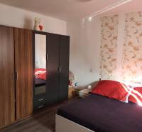 Na predaj 3-izb. rodinný dom, Gabčíkovo – Polná ulica - Spálňa v rodinnom dome s posteľou, vzorovanou tapetou, skrinkou a podlahou s dreveným dekorom.